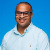 Miguel S. Hill smiling, wearing glasses and a light blue shirt.